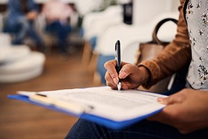Patient in waiting room filling out forms on clipboard