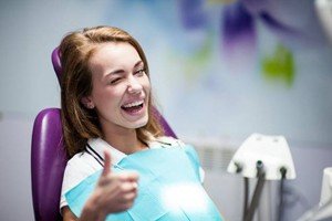 A woman smiling and giving a thumbs-up at her dental appointment