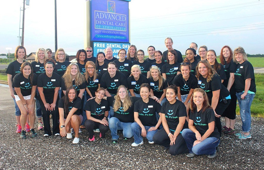 The whole team posing by Advanced Dental Care sign