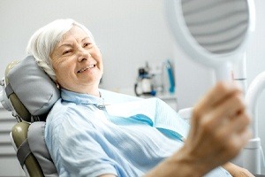 A woman smiling at herself in the mirror while in the dentist chair