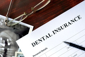 A dental insurance form with glasses, x-ray, pen, and money