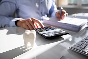 Hands button-pushing at desk with calculator and large model tooth