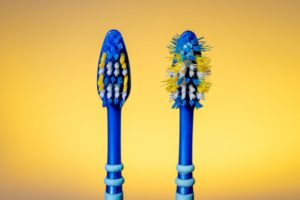 One new toothbrush and one used toothbrush on a yellow background