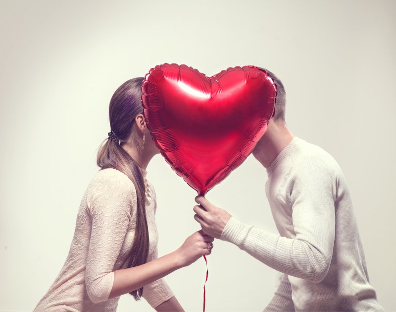 A couple kissing behind a balloon after receiving teeth whitening.