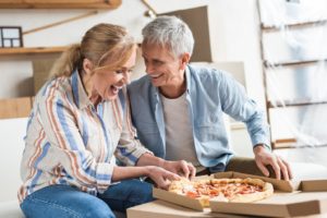 People with dentures eating a pizza and smiling.