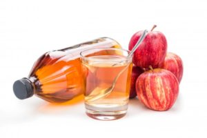 a bottle of apple cider vinegar in front of some fresh apples