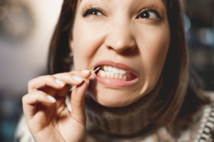 Woman squinting as she uses a toothpick to try and get food particles out from between her teeth