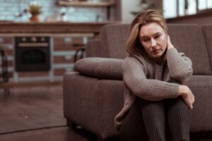 Woman sitting on the floor in front of a chair looking unhappy.